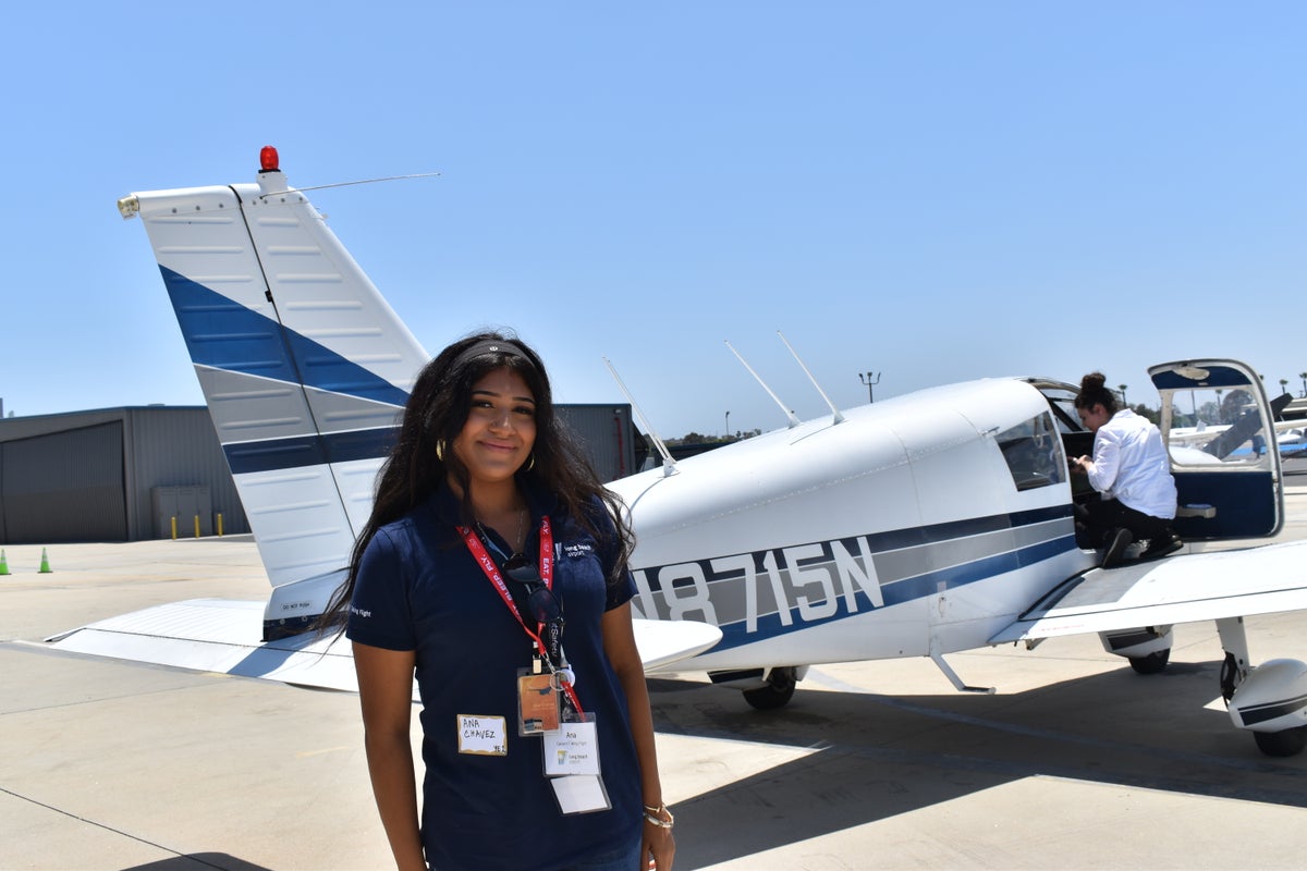 Student posing in front of a single engine plane.