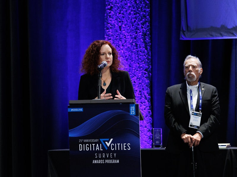 A woman stands at a podium with two men behind her. A woman stands at a podium with two men behind her.