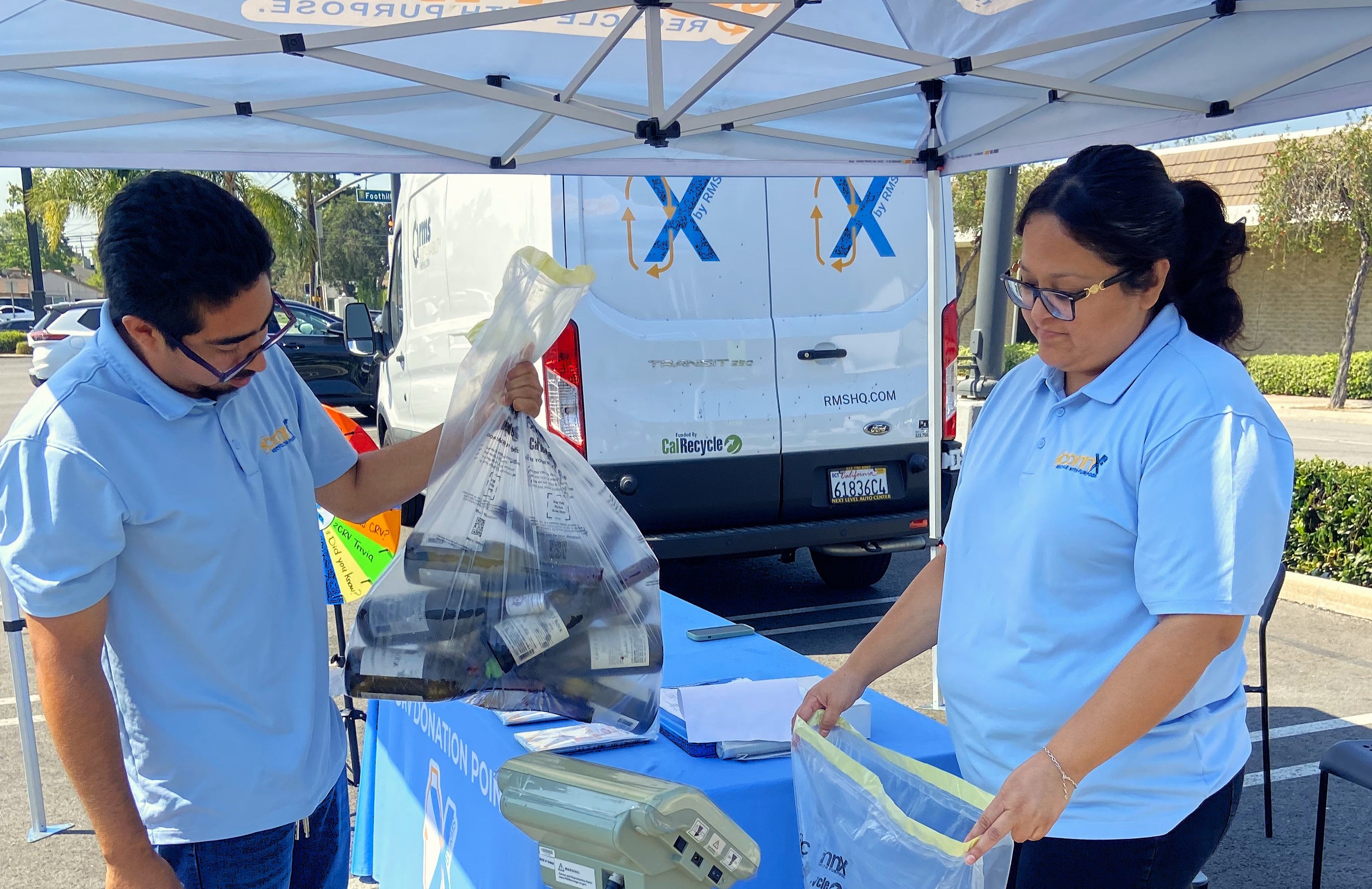 A man holding a plastic bag and a woman standing behind a table A man holding a plastic bag and a woman standing behind a table